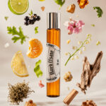 frasco de perfume âmbar de vidro modelo roll on com tampa cromada na posição vertical no centro rodeado por fatia de limão e laranja gomo de tangerina laranja madeira de cedro fava de baunilha hortelã