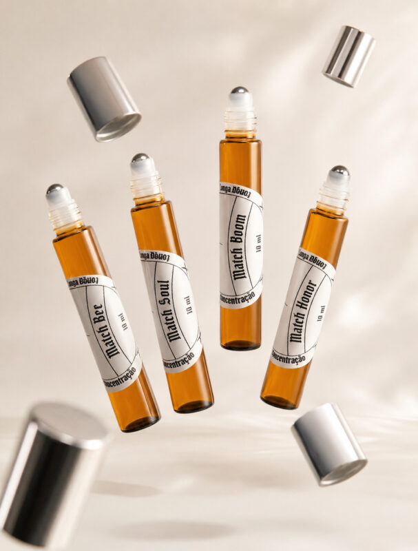 Quatro frascos cilíndricos de perfume de bolsa feitos com vidro âmbar e com pontas de aço deslizantes com rótulos brancos levitando lado a lado e tampas prateadas orbitando ao redor