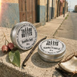 Duas latinhas de alumínio Matchii, com rótulos brancos redondos escritos Vanilla Soft e Vanilla Tropical, apoiadas sobre muro de concreto com baunilha, coco, folha e frutos ao redor.