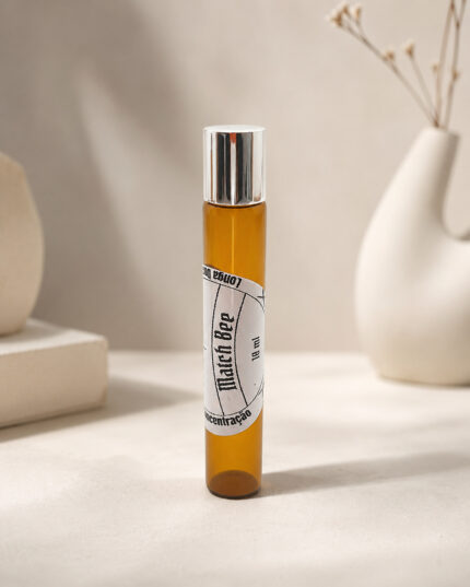 Frasco cilíndrico de perfume portátil feito em vidro âmbar com rótulo branco match bee na posição vertical sob pedra de granito bege