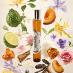 frasco cilíndrico de perfume de bolsa em vidro âmbar em posição vertical com tampa prateada rodeada por pedaços de pêssego limão âmbar laranja fava de baunilha fava tonka rosa jasmim lírio do campo lavanda