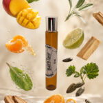 frasco âmbar de perfume roll on portátil posicionado vertical com elementos flutuantes ao redor manga tangerina fava tonka laranja limão hortelã